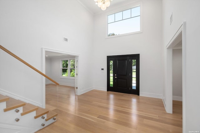 entrance foyer with a notable chandelier, ornamental molding, a high ceiling, and light hardwood / wood-style flooring