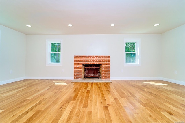 unfurnished living room with light hardwood / wood-style flooring, a healthy amount of sunlight, and a brick fireplace