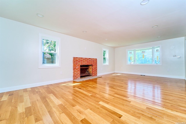 unfurnished living room with a brick fireplace, a wealth of natural light, and light wood-type flooring