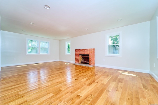 unfurnished living room with a fireplace, light hardwood / wood-style floors, and a healthy amount of sunlight