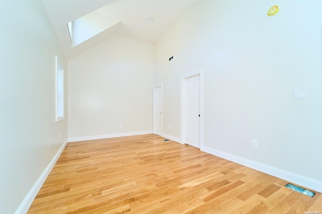 spare room featuring light hardwood / wood-style floors, high vaulted ceiling, and a skylight