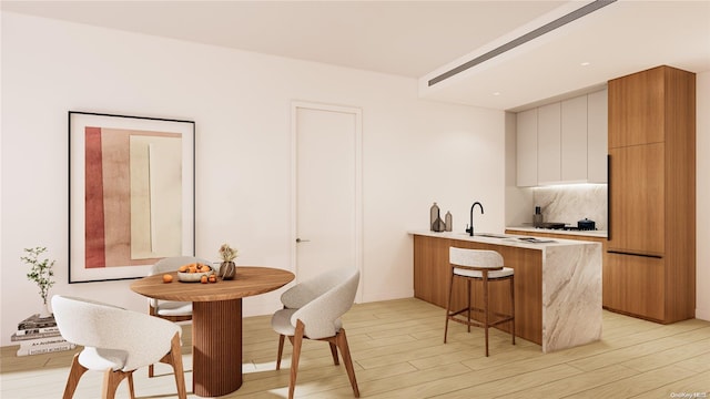 kitchen featuring backsplash, white cabinets, light wood-type flooring, a kitchen bar, and kitchen peninsula