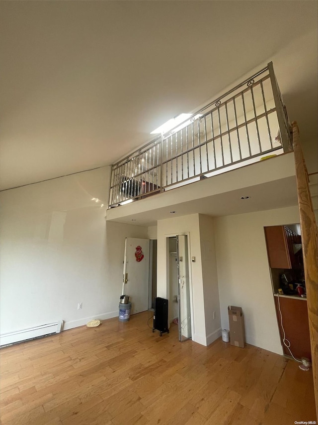 unfurnished living room with baseboard heating, a towering ceiling, and hardwood / wood-style flooring