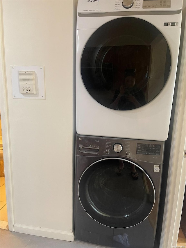 clothes washing area featuring stacked washing maching and dryer and light tile patterned floors