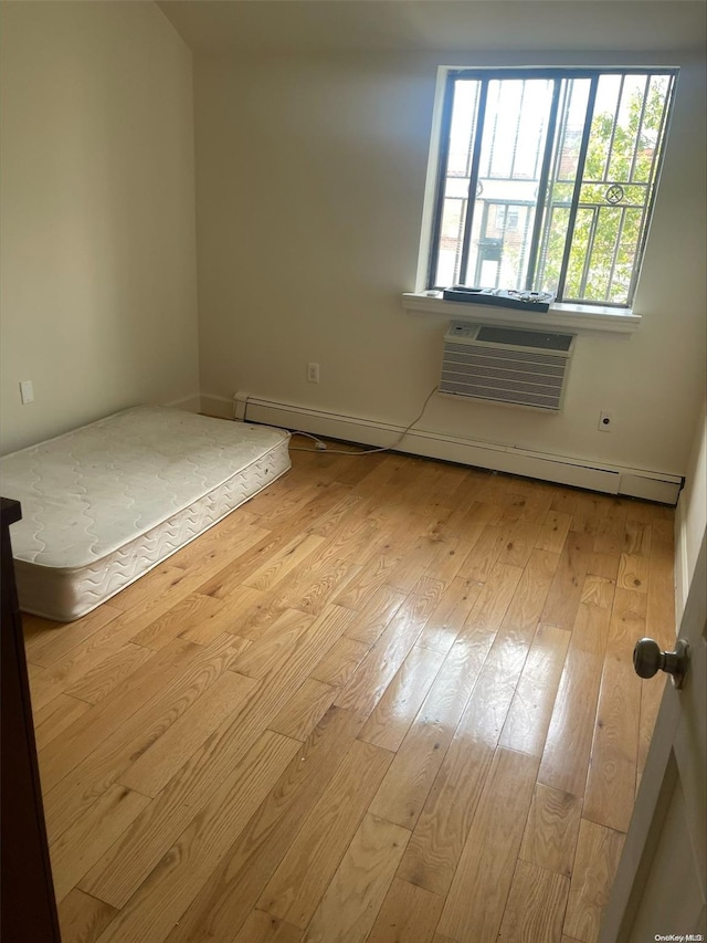 unfurnished bedroom with a baseboard radiator, light hardwood / wood-style flooring, and a wall unit AC