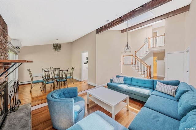 living room featuring beam ceiling, a wall mounted air conditioner, a brick fireplace, an inviting chandelier, and light hardwood / wood-style flooring