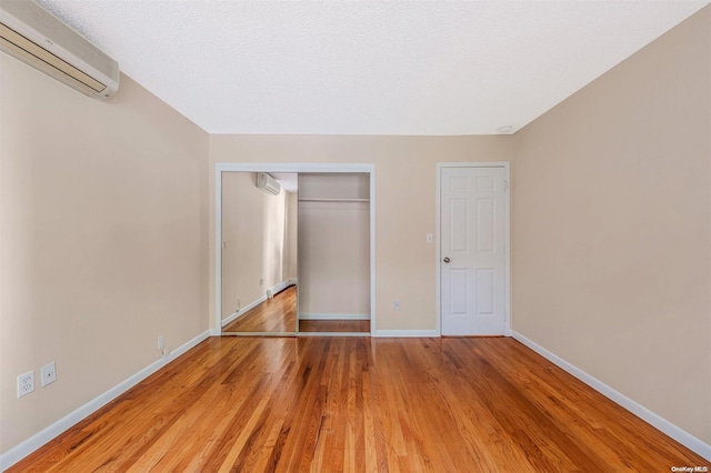 unfurnished bedroom featuring a closet, wood-type flooring, and a wall mounted AC