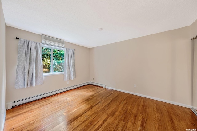 empty room featuring an AC wall unit, wood-type flooring, a textured ceiling, and a baseboard heating unit