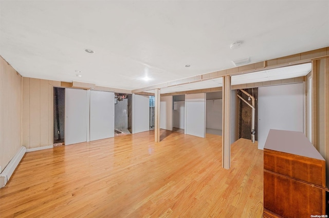 basement with light wood-type flooring, wooden walls, and a baseboard radiator