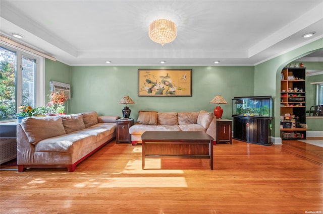 living room featuring a tray ceiling, ornamental molding, light hardwood / wood-style floors, and a notable chandelier