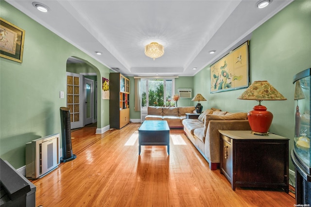 living room with light hardwood / wood-style floors, an inviting chandelier, a wall mounted AC, and a tray ceiling