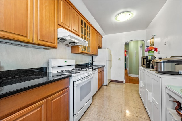 kitchen featuring dark stone countertops, white appliances, range hood, and sink