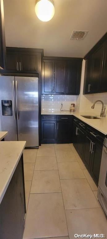 kitchen with stainless steel fridge, sink, light tile patterned floors, and light stone counters