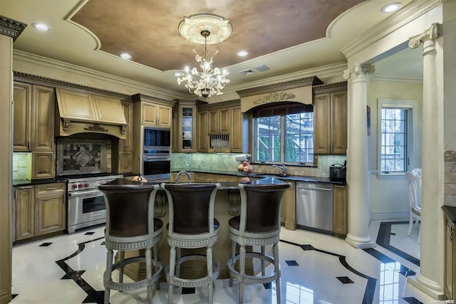 kitchen featuring an island with sink, appliances with stainless steel finishes, tasteful backsplash, custom range hood, and decorative columns