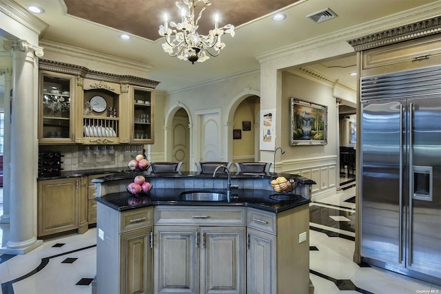 kitchen with built in refrigerator, a kitchen island with sink, sink, and crown molding