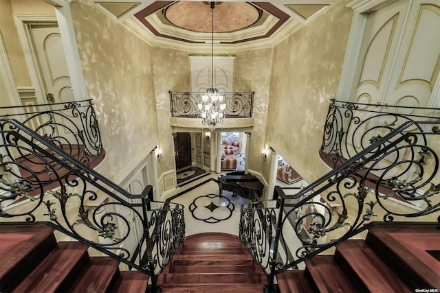 stairs featuring a high ceiling, hardwood / wood-style flooring, ornamental molding, a tray ceiling, and a chandelier