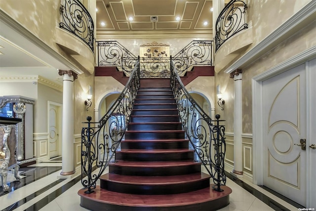 staircase featuring tile patterned floors, a towering ceiling, ornate columns, and ornamental molding