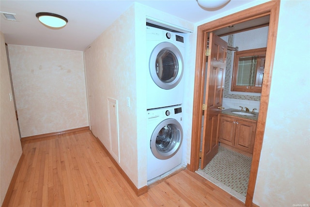 clothes washing area with stacked washer / drying machine, light wood-type flooring, and sink