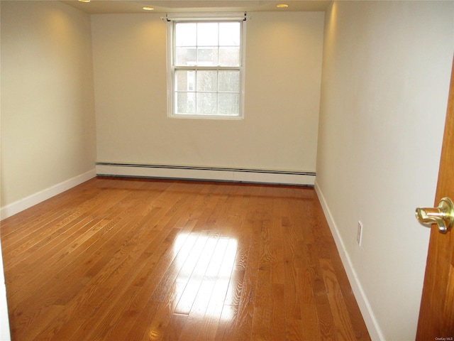 unfurnished room featuring hardwood / wood-style flooring and a baseboard heating unit