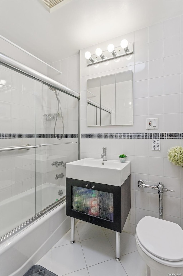 full bathroom with combined bath / shower with glass door, vanity, tile walls, tile patterned flooring, and toilet