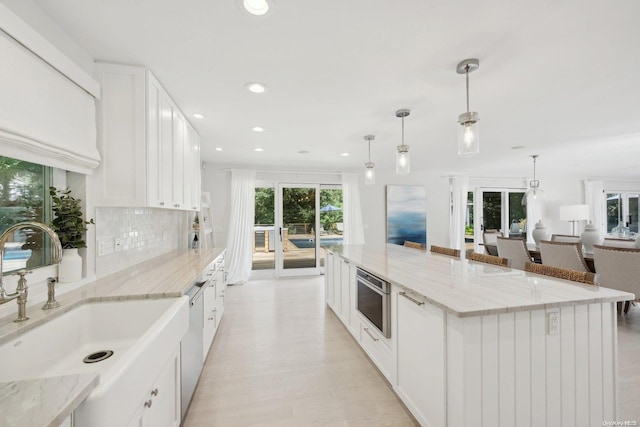 kitchen with white cabinetry, sink, light stone counters, and decorative light fixtures