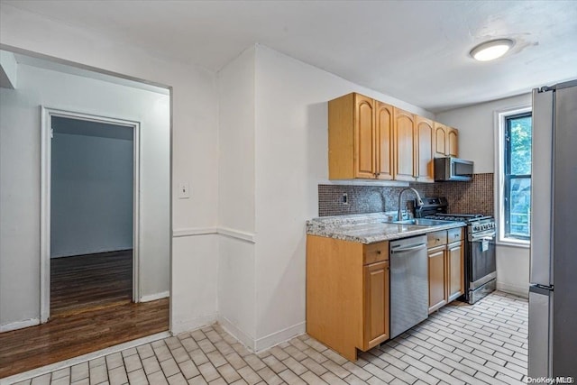 kitchen featuring light stone countertops, sink, backsplash, appliances with stainless steel finishes, and light wood-type flooring