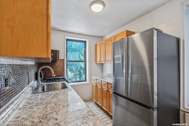 kitchen with stainless steel refrigerator, sink, light stone counters, backsplash, and light tile patterned floors