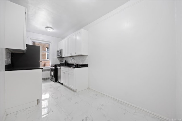 kitchen featuring radiator, white cabinetry, sink, decorative backsplash, and appliances with stainless steel finishes