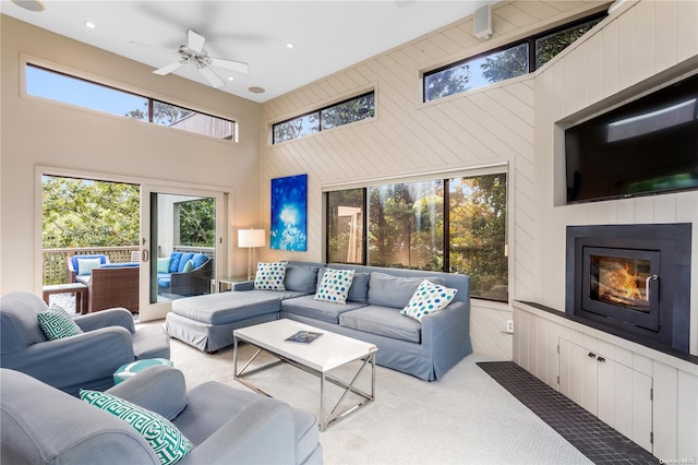 carpeted living room with wooden walls, ceiling fan, and a high ceiling