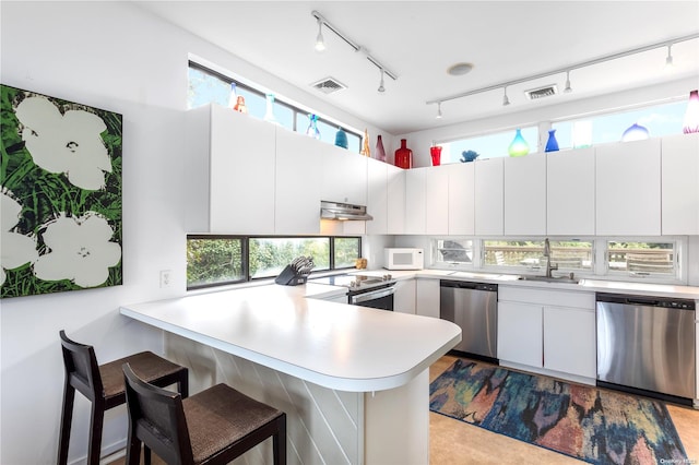 kitchen with white cabinetry, a kitchen bar, kitchen peninsula, and stainless steel appliances