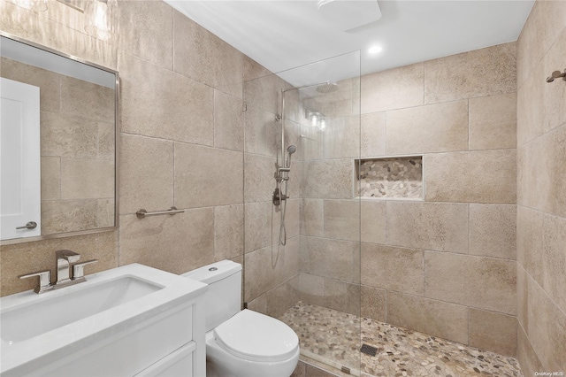 bathroom featuring tiled shower, vanity, toilet, and tile walls