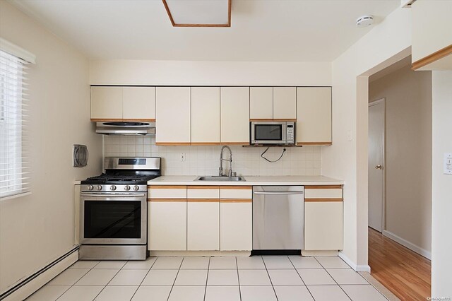 kitchen with sink, stainless steel appliances, a baseboard radiator, extractor fan, and decorative backsplash