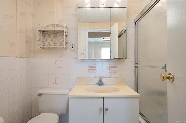 bathroom with vanity, toilet, tile walls, and walk in shower