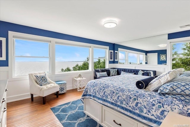 bedroom featuring multiple windows, a water view, and hardwood / wood-style flooring