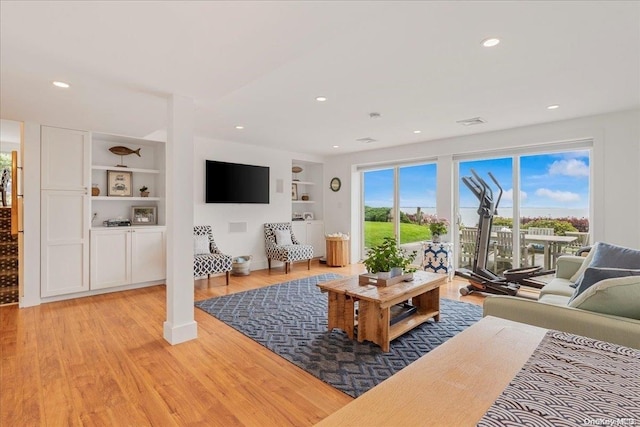 living room featuring built in shelves, light hardwood / wood-style floors, and a wealth of natural light