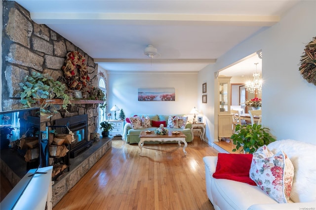 living room with beamed ceiling, hardwood / wood-style floors, a stone fireplace, and a notable chandelier