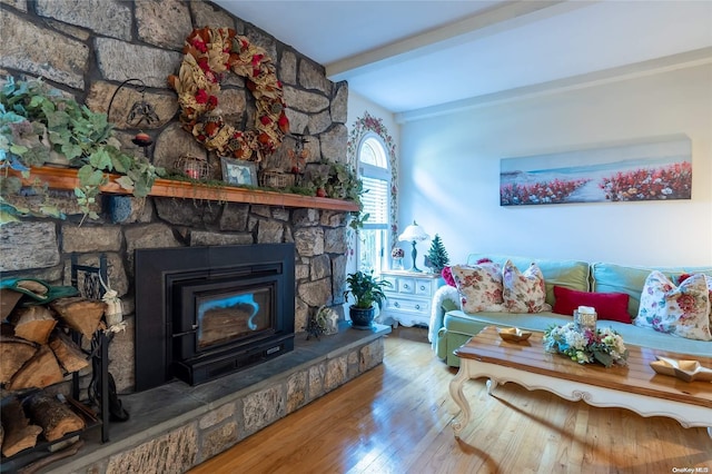 living room with beamed ceiling, a stone fireplace, and wood-type flooring