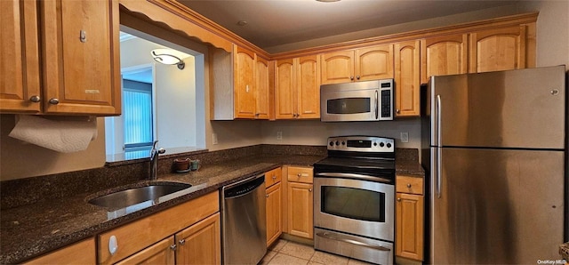 kitchen with sink, light tile patterned floors, dark stone counters, and appliances with stainless steel finishes