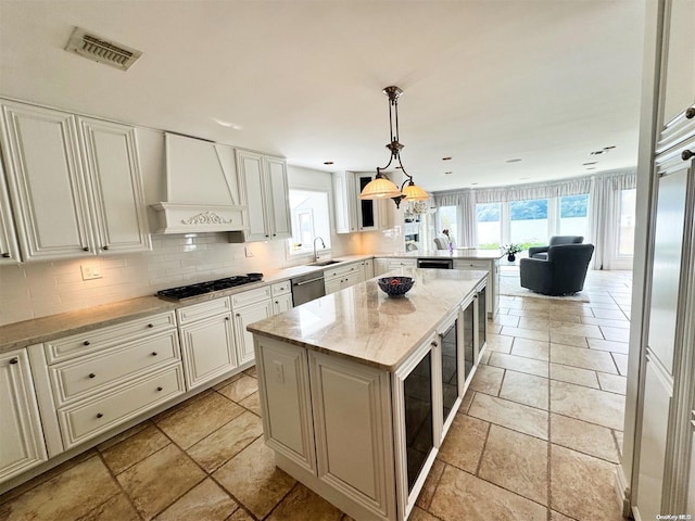 kitchen featuring light stone countertops, a center island, hanging light fixtures, premium range hood, and appliances with stainless steel finishes