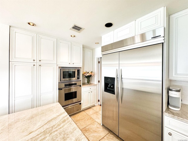 kitchen featuring built in appliances, white cabinetry, light tile patterned floors, and light stone counters