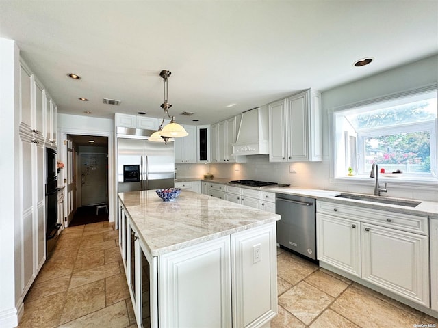 kitchen with sink, a center island, hanging light fixtures, custom range hood, and appliances with stainless steel finishes