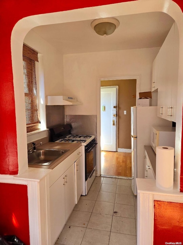 kitchen featuring white appliances, exhaust hood, sink, light tile patterned floors, and white cabinetry