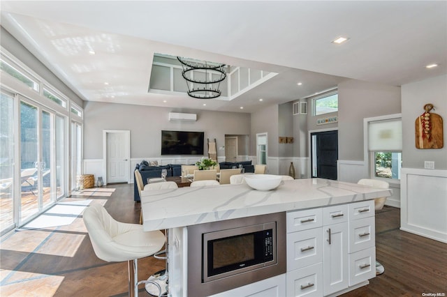 kitchen featuring stainless steel microwave, white cabinets, a kitchen breakfast bar, a kitchen island, and light stone counters