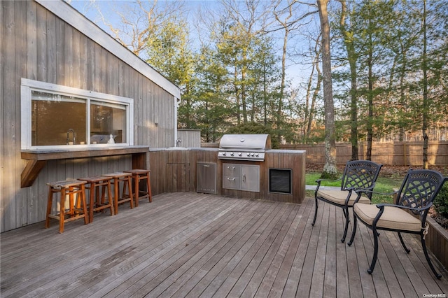 wooden terrace with an outdoor kitchen, area for grilling, and a bar