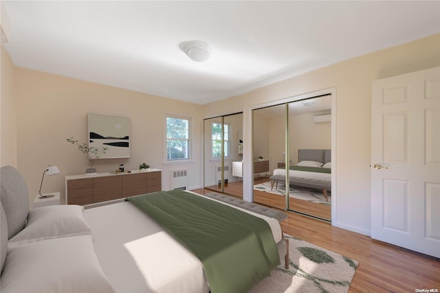 bedroom with light hardwood / wood-style floors, an AC wall unit, radiator, and two closets