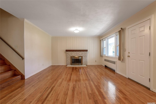 unfurnished living room with light hardwood / wood-style floors, radiator heating unit, ornamental molding, and a brick fireplace