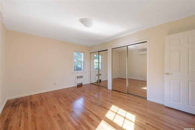 unfurnished bedroom featuring radiator, a wall mounted AC, light hardwood / wood-style floors, and two closets