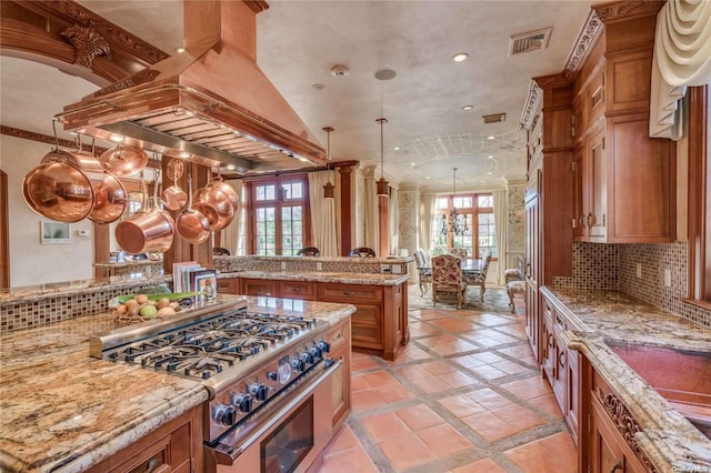 kitchen with french doors, hanging light fixtures, high end stainless steel range oven, backsplash, and custom range hood