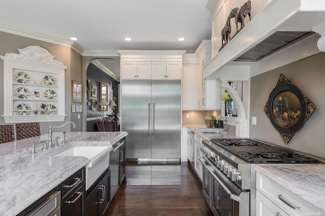 kitchen with light stone countertops, ornamental molding, high end appliances, dark wood-type flooring, and white cabinets