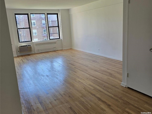 empty room featuring radiator, a wall mounted air conditioner, baseboards, and wood finished floors